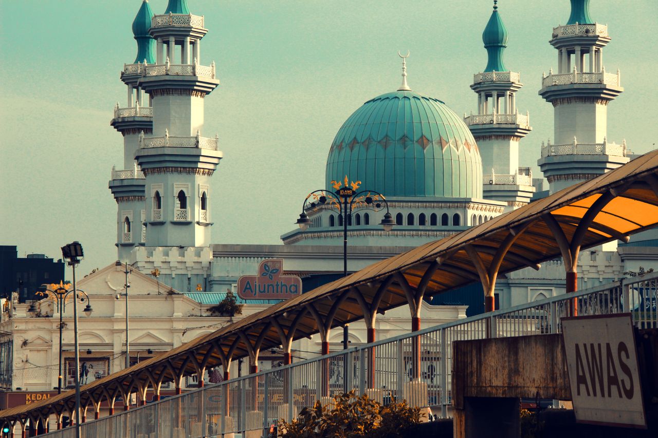 A stunning view of a mosque with aqua domes and towering minarets, set against an urban backdrop.
